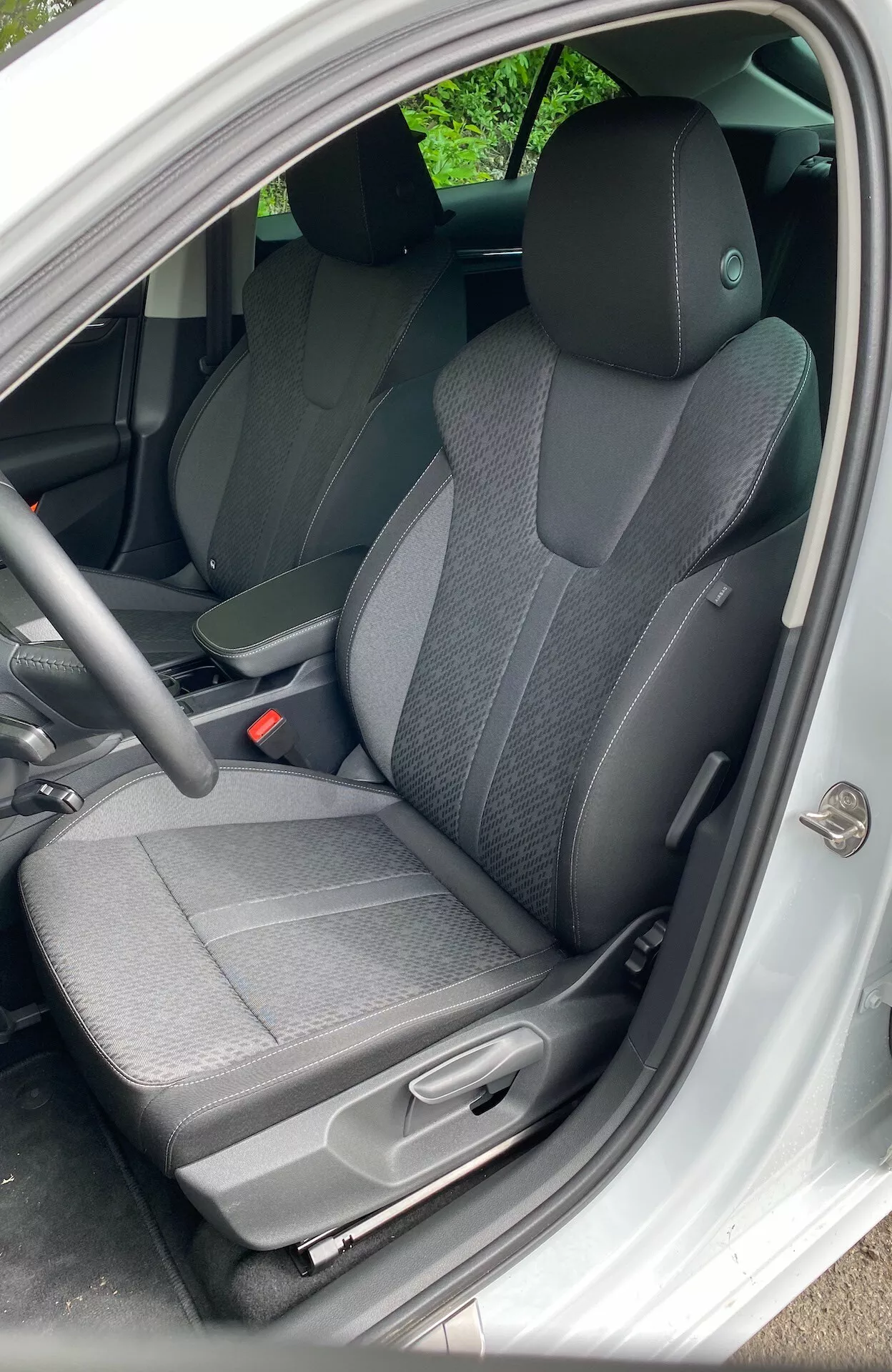 2020-as Škoda Octavia Limousine belső kilátás a vezetőoldalról nyitott ajtóval. Két tónusú szövetülés, egyszerű műszerfal, standard kormánykerék, sötét szőnyeg, kézi ülésállítás és alapvető beltér kialakítás.