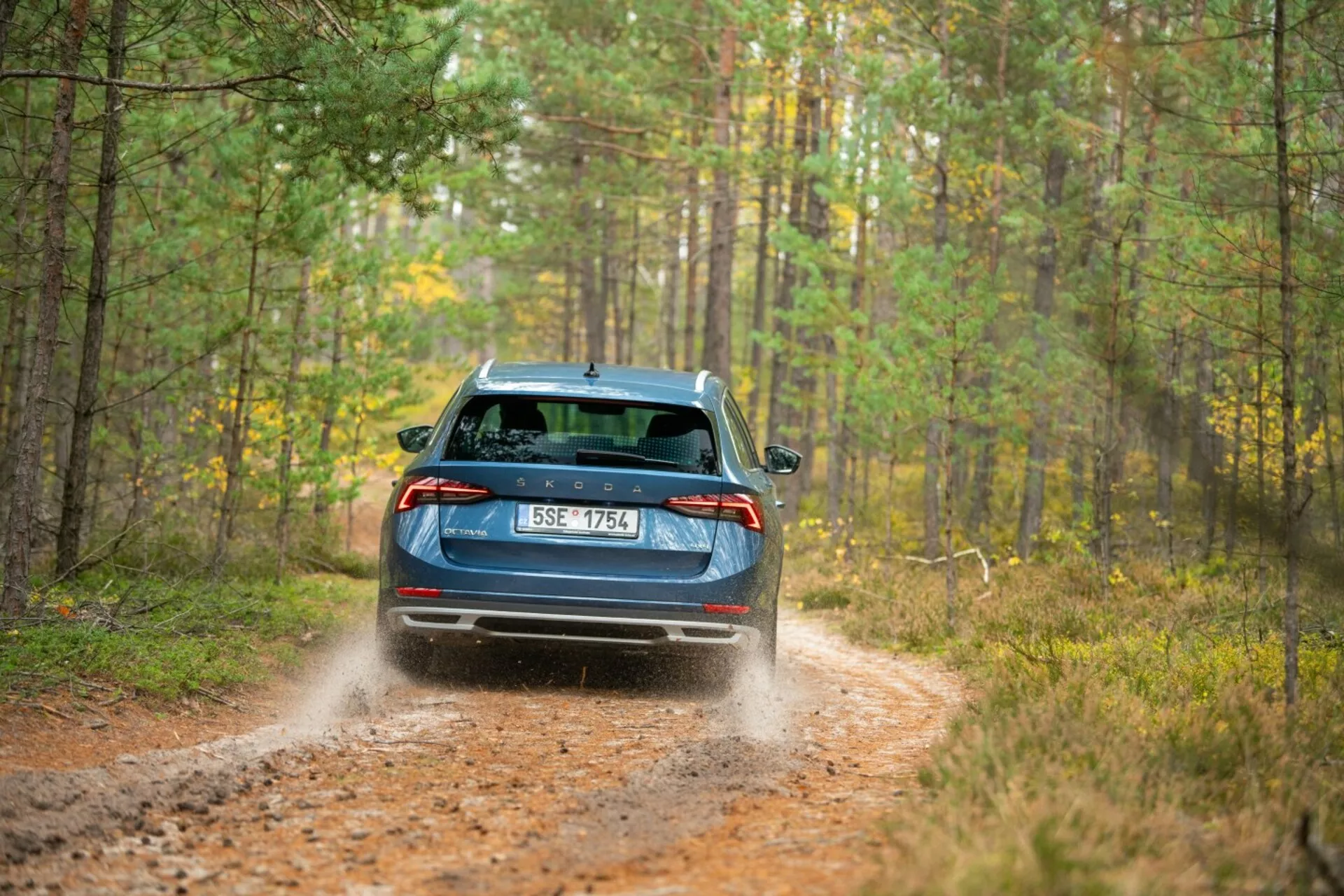 2017-es kék Skoda Octavia limuzin, LED-es hátsó lámpákkal, hátsó ablaktörlővel és kettős kipufogóval erdei úton, dinamikusan felpörgő porral jelezve az összkerékhajtás képességeit