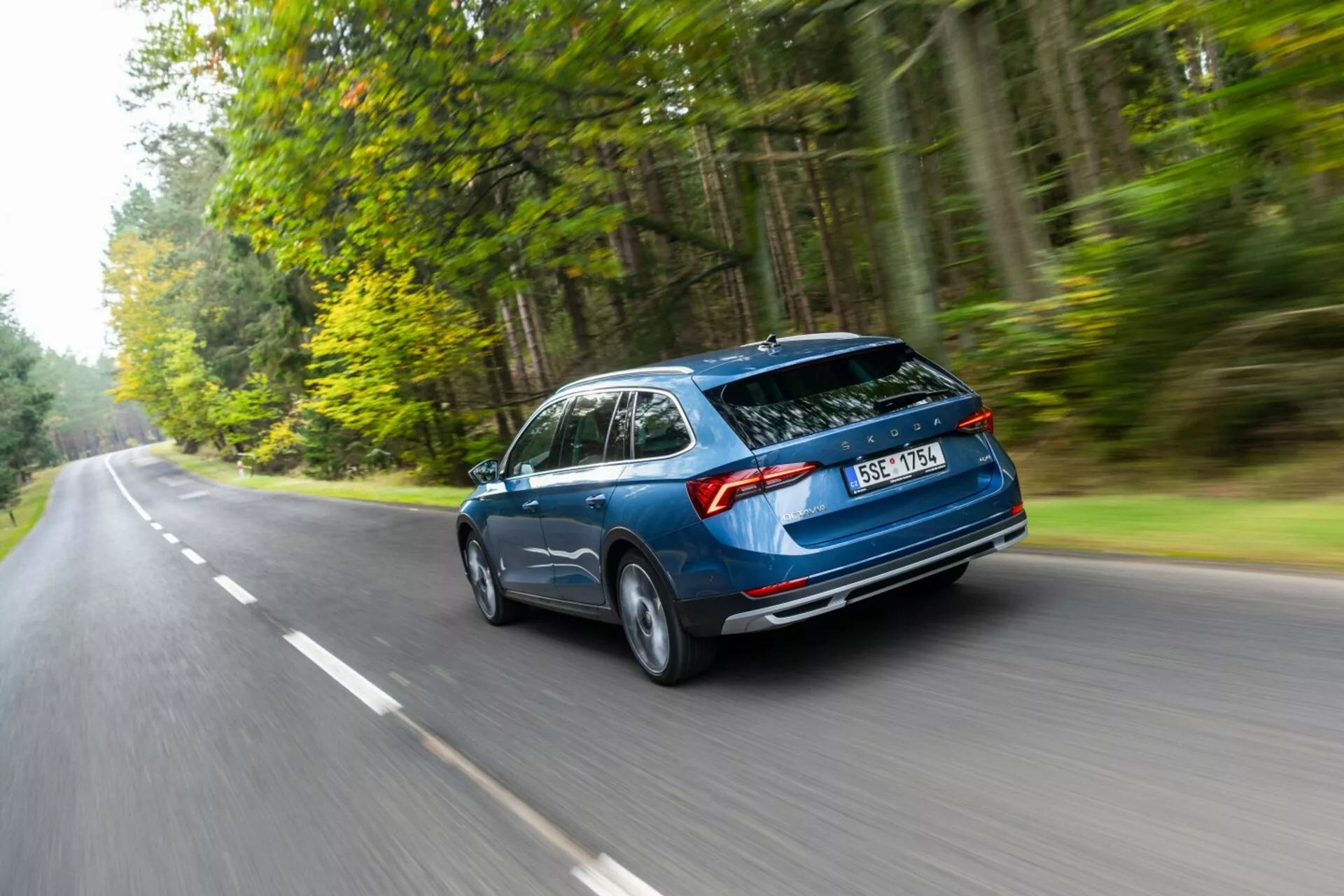 2017-es Skoda Octavia kombi menet közben, háromnegyedes hátsó szögből rögzítve, kiemelve az aerodinamikus tervezést, a hátsó hatchback csomagtartót és a vízszintes hátsó lámpákat egy erdővel szegélyezett úton