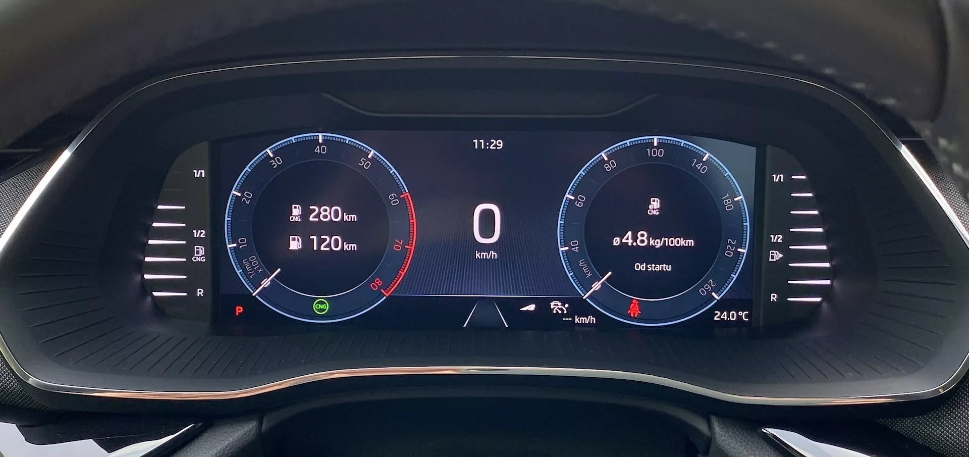 Közelkép a Škoda Octavia 2020 digitális műszerfalról vezetői perspektívából, szélesvásznú kijelzővel fekete háttérrel és élénk digitális grafikával. A bal oldalon egy fordulatszámmérő látható 8 000 RPM-ig, 6 500 RPM-től piros jelzéssel, a mutató alapjáraton. Középen a sebesség '0 km/h', az óra '11:29', az üzemanyag-fogyasztás '4,8 l/100km' és a megtett távolság '6540 km' látható. A jobb oldalon egy sebességmérő grafikonral és 280 km/h jelzéssel, valamint '24°C' hőmérséklettel. Ikonok között van egy navigációs iránytű és egy üzemanyagszint-jelző.