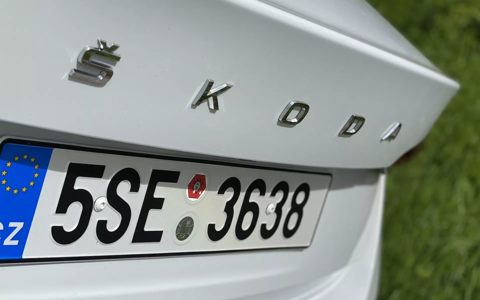 Közelkép a Škoda Octavia 2020 limuzin hátsó részéről, amely a csomagtérajtóra, a hátsó rendszámtáblára az európai 'CZ' azonosítóval, valamint a krómozott 'SKODA' feliratra összpontosít. A jellemzők között négy kör alakú parkolószenzor található a rendszámtábla felett, hogy segítsék a jármű manőverezését.