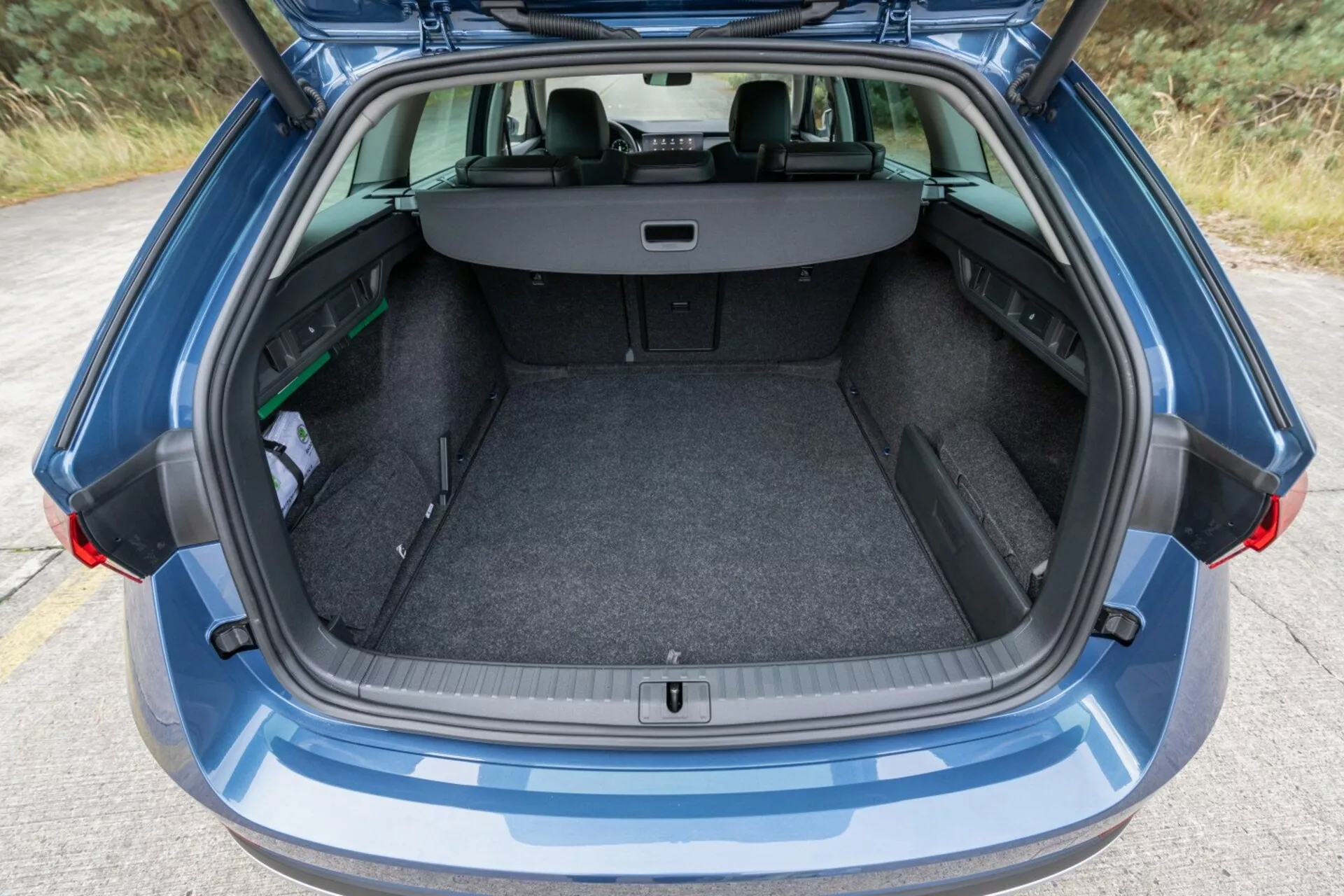 2017-es Skoda Octavia Limuzin hátsó nézete, kiemelve a tágas, tiszta csomagtartóját nyitott csomagtér-ajtóval, visszahúzható csomagtartó-fedéllel, és látható 60/40 felosztású hátsó ülések konfigurációját a megnövelt csomagtér-kapacitás érdekében, mellette egy kis esernyő és egy zöld tárgy, környezeti fényben.