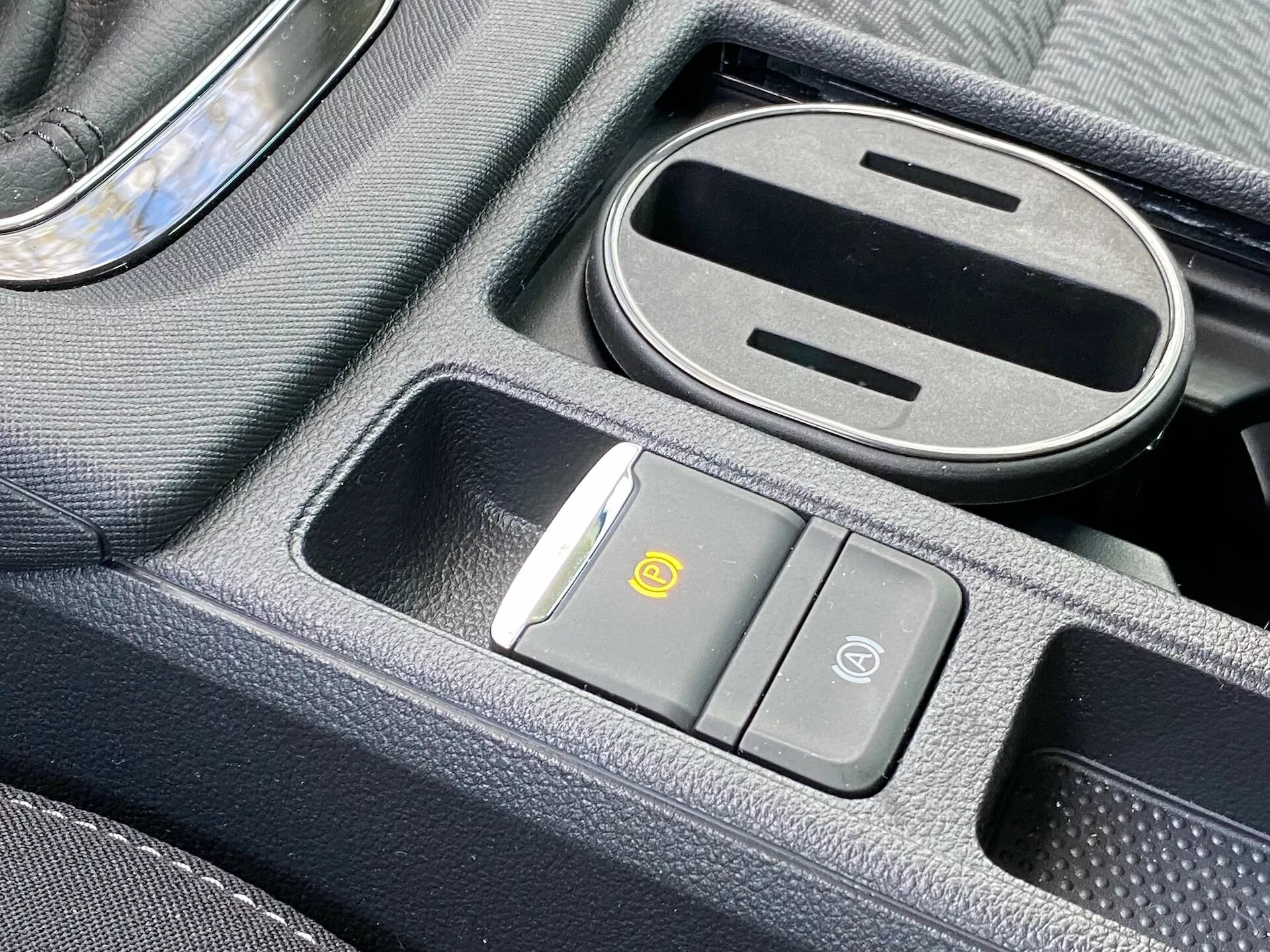 Közelkép a 2020-as Skoda Octavia középkonzoljáról, amely tartalmaz egy vezeték nélküli töltőpadot, légáramlat szabályozó gombot, járműbiztonsági gombot, részben nyitott gumibetétes tárolórekeszt és króm díszes váltókart.