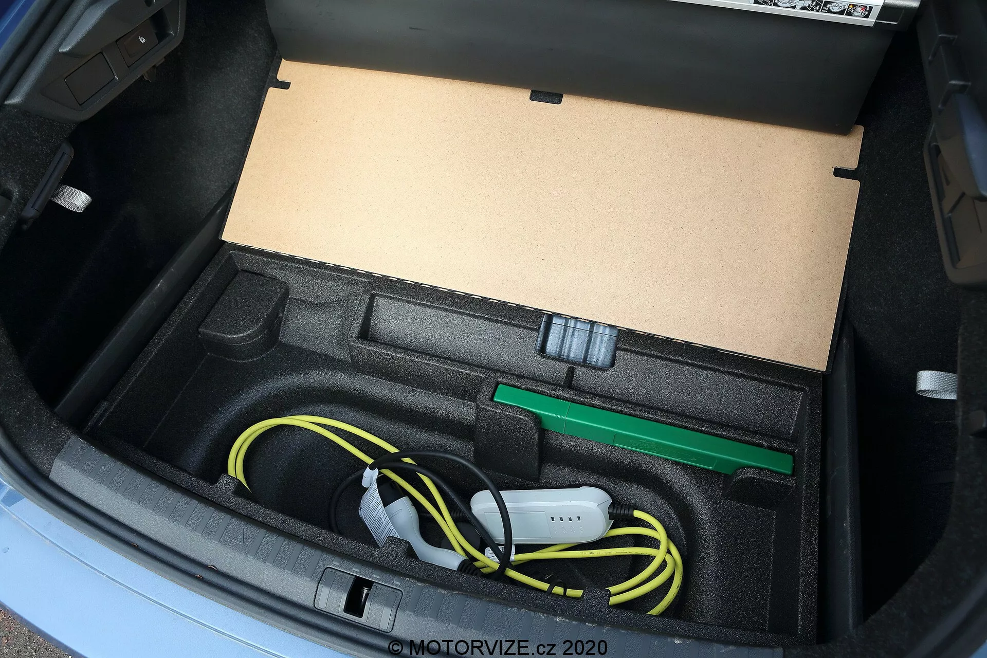 A 2020-as Skoda Octavia csomagtartójának közeli nézete, amely a villamos jármű töltőkábelének és tartozékainak tárolására tervezett egyedi rekeszt mutatja, beleértve a gondosan feltekert sárga töltőkábelt és a zöld vontatószemet, magas szögből, természetes fényben rögzítve.