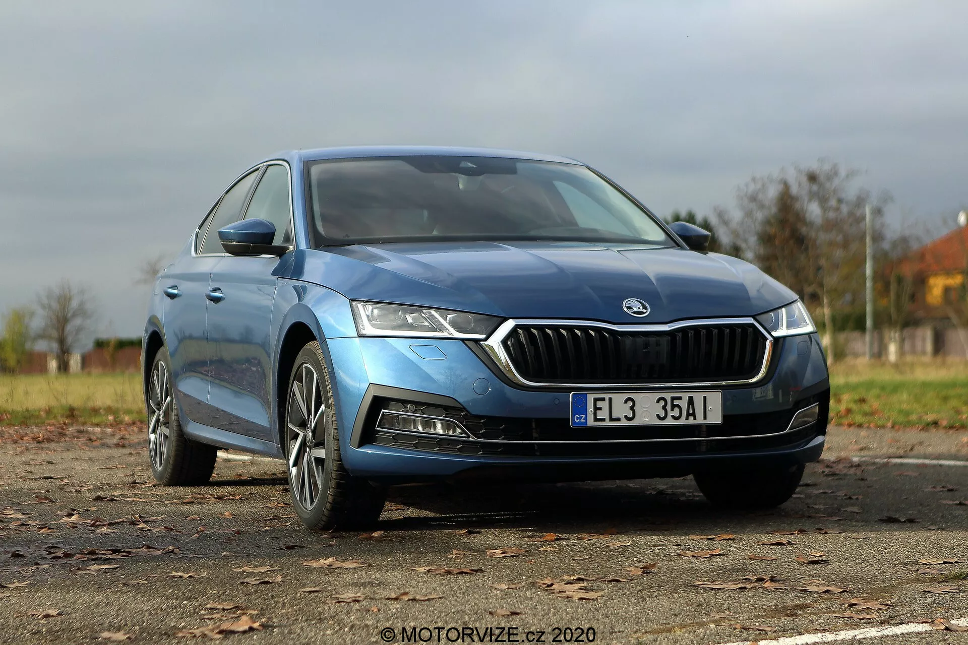 A képen egy kék 2020-as Škoda Octavia Limousine látható alacsony elülső háromnegyed szögből, kiemelve az egyedi krómozott elülső rácsot, éles LED fényszórókat, kontúros motorháztetőt, modern könnyűfém kerekeket és stílusos oldal tükröket beépített indexekkel. A sima karosszéria és az enyhén sötétített, keret nélküli ablakok magasabb felszereltségi szintet sugallnak, miközben az autó teljes hossza látható, beleértve a modellt vagy motor típusát jelző jelvényeket.