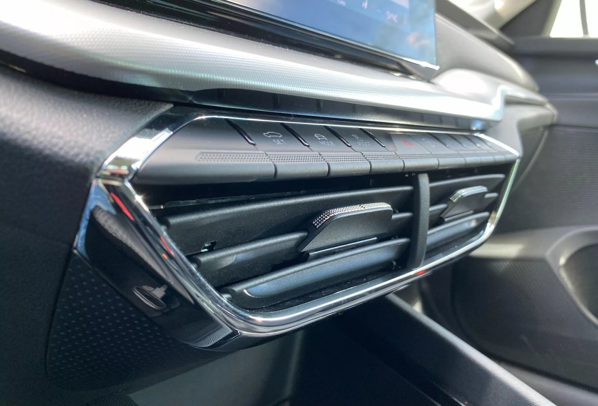 Közelkép a Skoda Octavia 2020 belsejéről, kiemelve a légkondicionáló szellőzőnyílást és a műszerfal környező területét, modern szellőzőnyílás-kialakítással, króm akcentusokkal és alul érintésérzékeny klímaberendezés gombokkal, puha tapintású és szénszálas hatású műszerfallal.