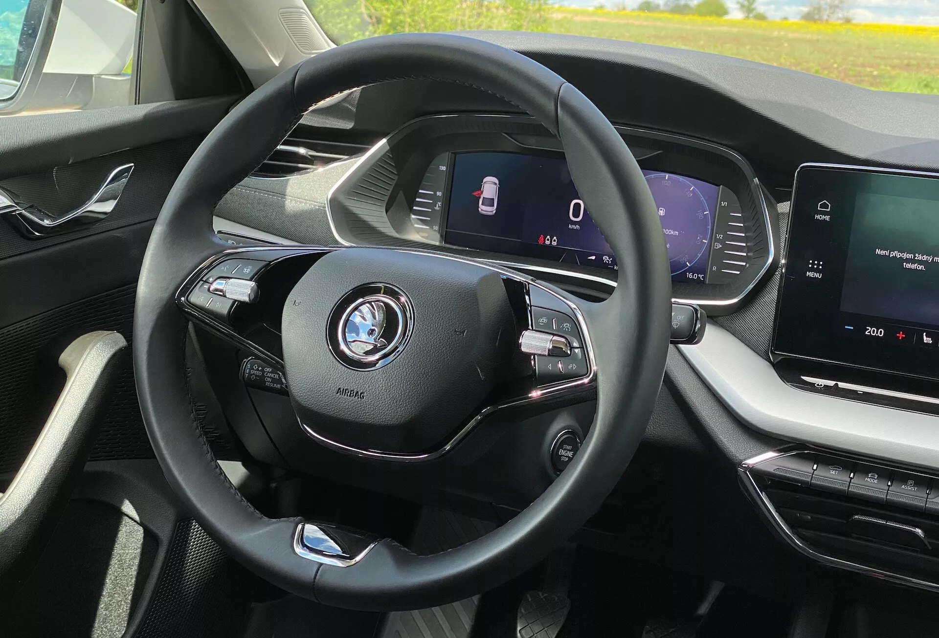 A Skoda Octavia 2020 belső nézete a vezető ülésének perspektívájából; középpontban modern háromküllős kormánykerék többfunkciós vezérlőkkel a média és a telefon számára, látható autó embléma; teljesen digitális műszerfal, amely sebességet és biztonsági funkciókat, például sávasszisztenst jelenít meg; középkonzol infotainment érintőképernyővel, amely a médiarendszert és esetleg a navigációt mutatja; modern, felső kategóriás belső tér tiszta vonalakkal és jól megtervezett szellőzőnyílásokkal; nincs külső kilátás, csak a vezető közvetlen környezete a kabinban; fejlett autós technológiai jellemzők jelei, mint például az adaptív sebességtartó automatika és a csatlakozási funkciók.