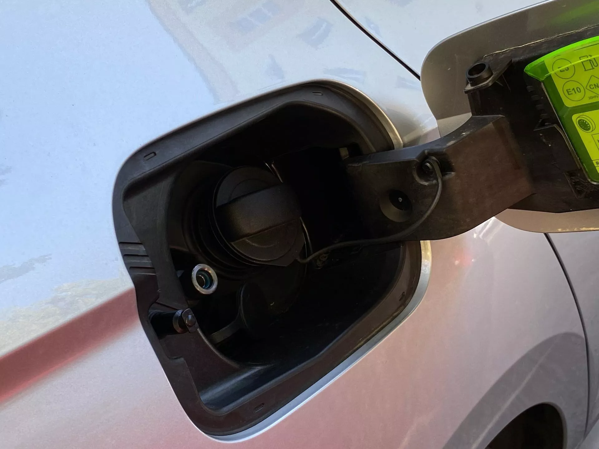 Közelkép a 2020-as Skoda Octavia Limousine üzemanyagtöltő területéről, ahol a nyitott tanksapka rugalmas szíjjal van rögzítve, a jármű karosszériájának környező részletei és a süllyesztett üzemanyagtöltő nyakban látható szelep látható, mindezt enyhén lefelé mutató szögből nézve.