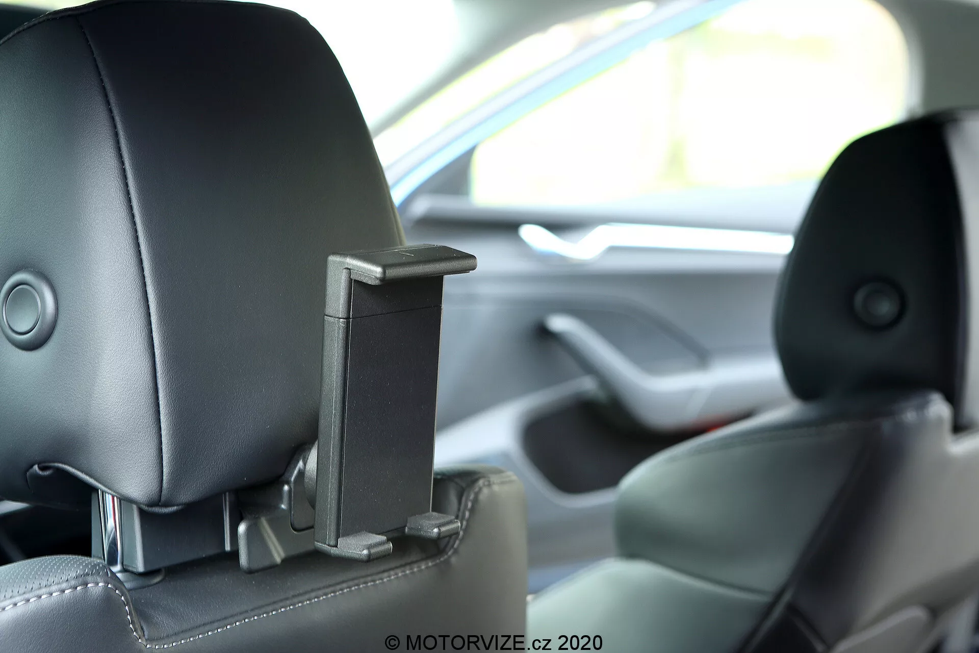 Egy 2020-as Skoda Octavia belső tere, amely a hátsó középső fejtámlát mutatja egy beépített, visszahúzható elemmel, valószínűleg szórakoztató vagy biztonsági funkcióval. A kép a hátsó utas szemszögéből tekintve szemmagasságban rögzíti a fejtámlát, sekély mélységű élességgel, bemutatva a kéttónusú bőr kárpitot és kiemelve az előrehaladott technológiai és ergonómiai tervezést.