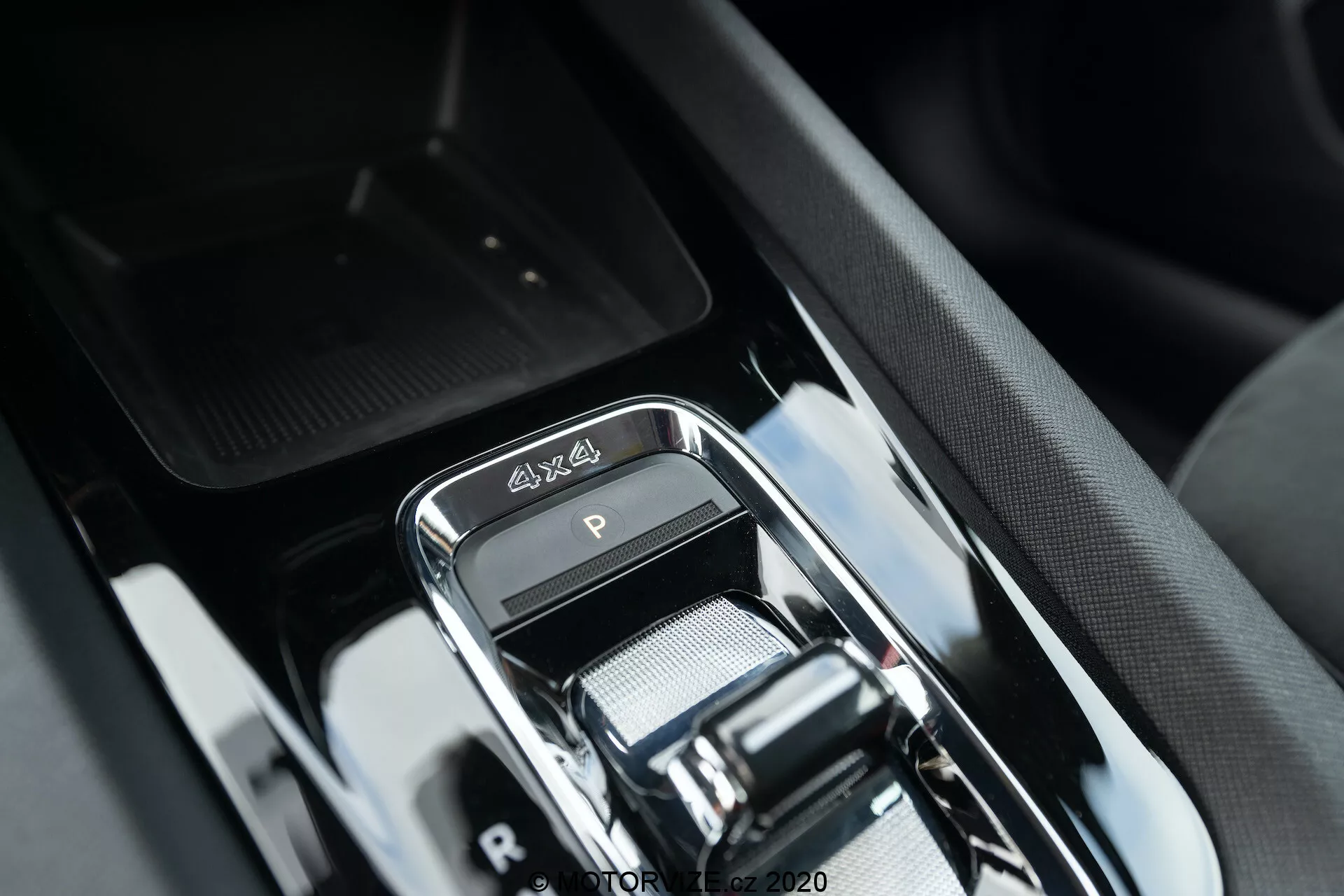 Közeli kép a 2020-as Skoda Octavia Scout luxus belterének váltóterületéről, amely modern elektronikus krómozott váltókart, 4x4 emblémát, elegáns magas fényű fekete díszítést és kifinomult középkonzol kialakítást mutat, környező gombokkal és egy rejtett tárolórekesszel.