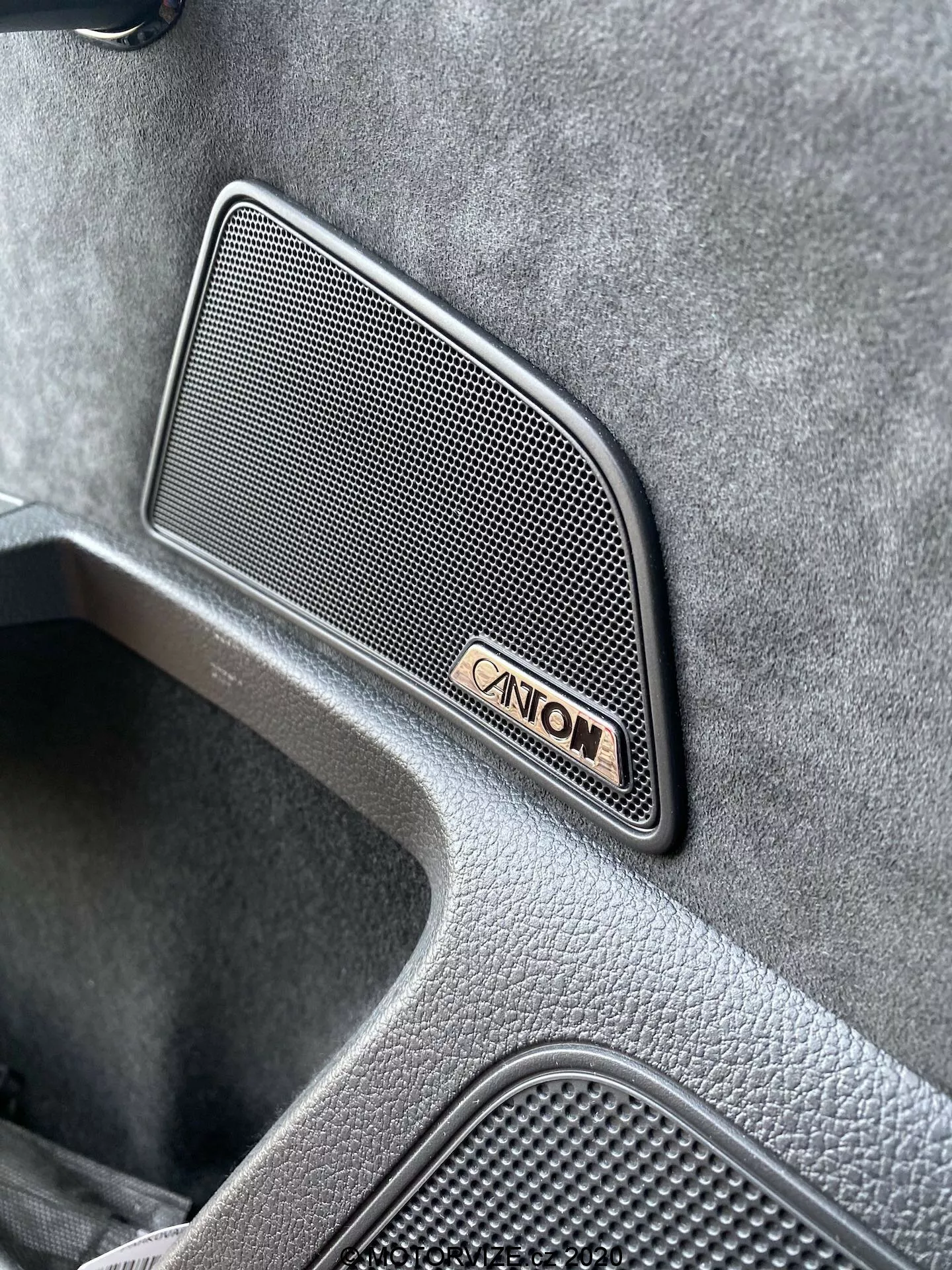 Közelkép szögből a 2019-es Skoda Superb Limousine belteréről, kiemelve egy premium Canton hangszóró rácsot hálós mintával, amely trapéz alakú és az ajtópanelemre van szerelve, a Canton jelvénnyel kísérve, amely egy csúcsminőségű texturált felületet és egy süllyesztett részt mutat, amely egy luxus jármű designjára utal.