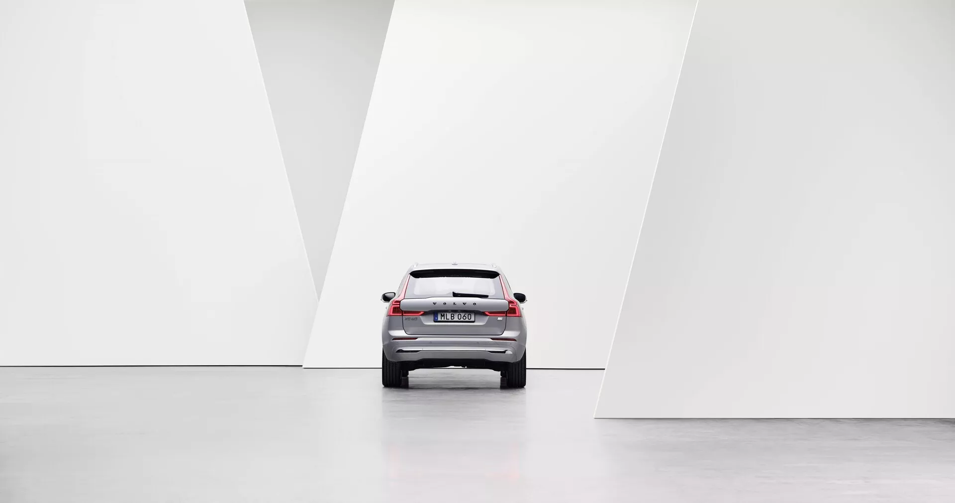 Autó hátulnézeti perspektívából, modern designelemekkel, beleértve LED hátsó lámpák, hátsó szélvédő, csomagtérajtó és hátsó lökhárítóot minimalista, világos és szimmetrikus környezetben, fényes padlóval és geometrikus fehér falakkal.