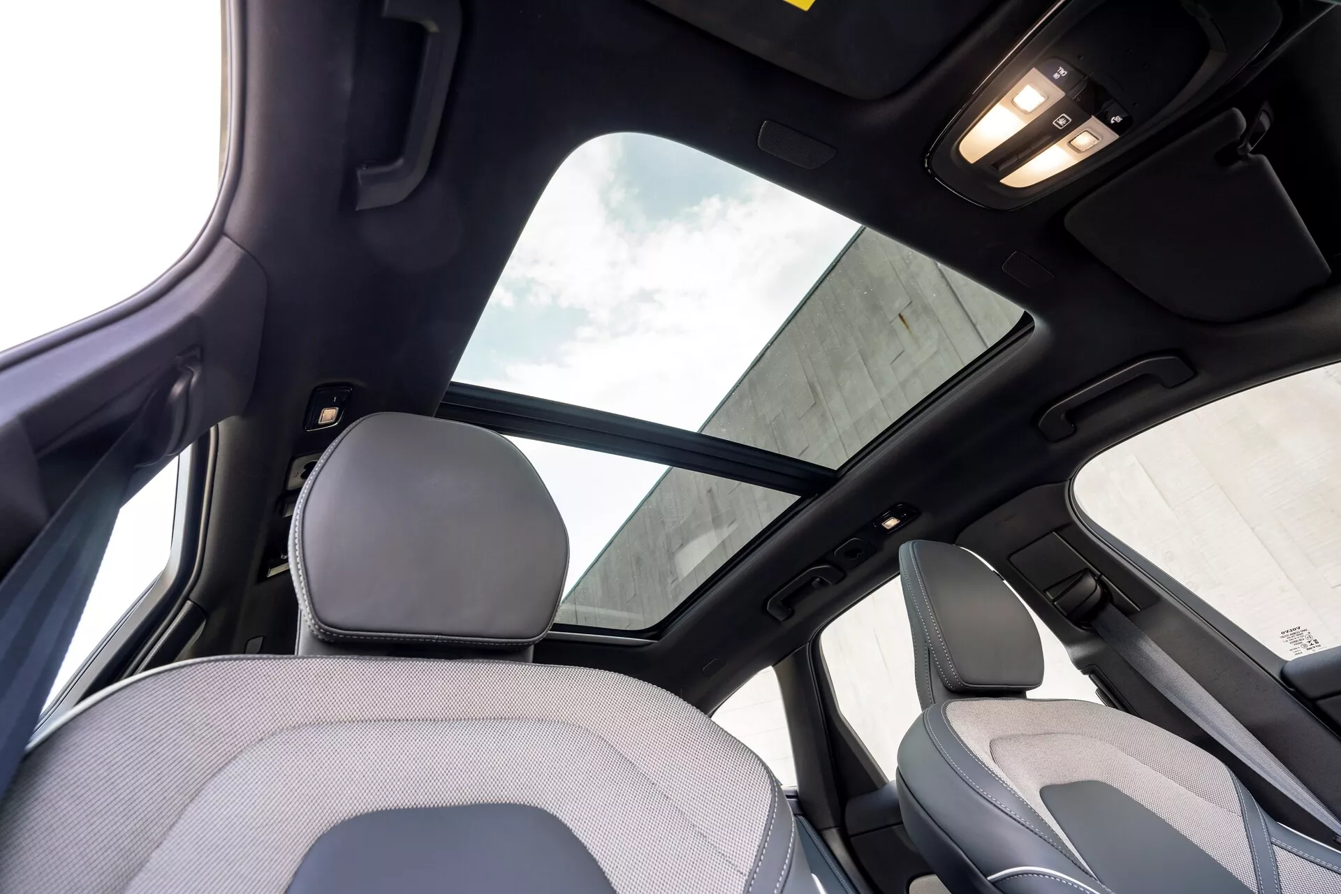 A 2021-es Volvo XC60 második generációs facelift belseje, hátsó ülés nézetből, a kabin felső részére összpontosítva. Figyelemre méltó jellemzők közé tartozik a nagy panoráma napfénytető árnyékolóval, fekete tetőkárpit, amely magasabb felszereltségi szintre vagy luxuscsomagra utal, és a kabinvilágítás a mennyezeten. A képen látható az első utasülés fejtámlájának és felső háttámlájának egy része, valamint az oldaloszlop és a hátsó ajtó feletti fogantyú.