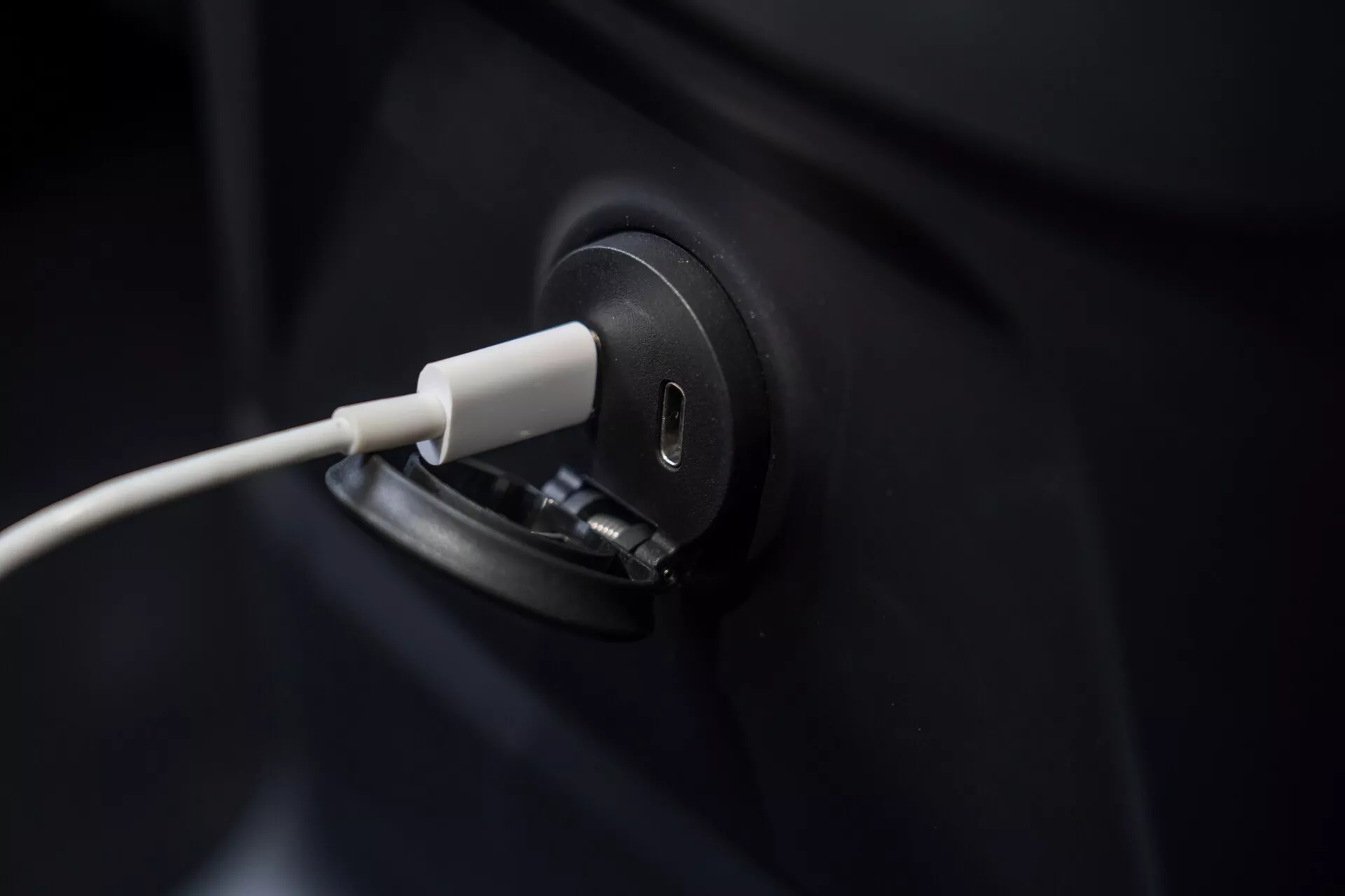 Közelkép egy Volvo XC60 2021-es elektromos jármű töltőportjáról csatlakoztatott kábel mellett, kiemelve a karcsú és modern dizájnt. A kép szorosan a töltőportra összpontosít, így az autó sötét színű teste nagyrészt nem látható. Az elmosódott háttér hangsúlyozza az EV töltési folyamatának pontosságát, ami a zöld technológiát és a fenntartható közlekedést szimbolizálja.