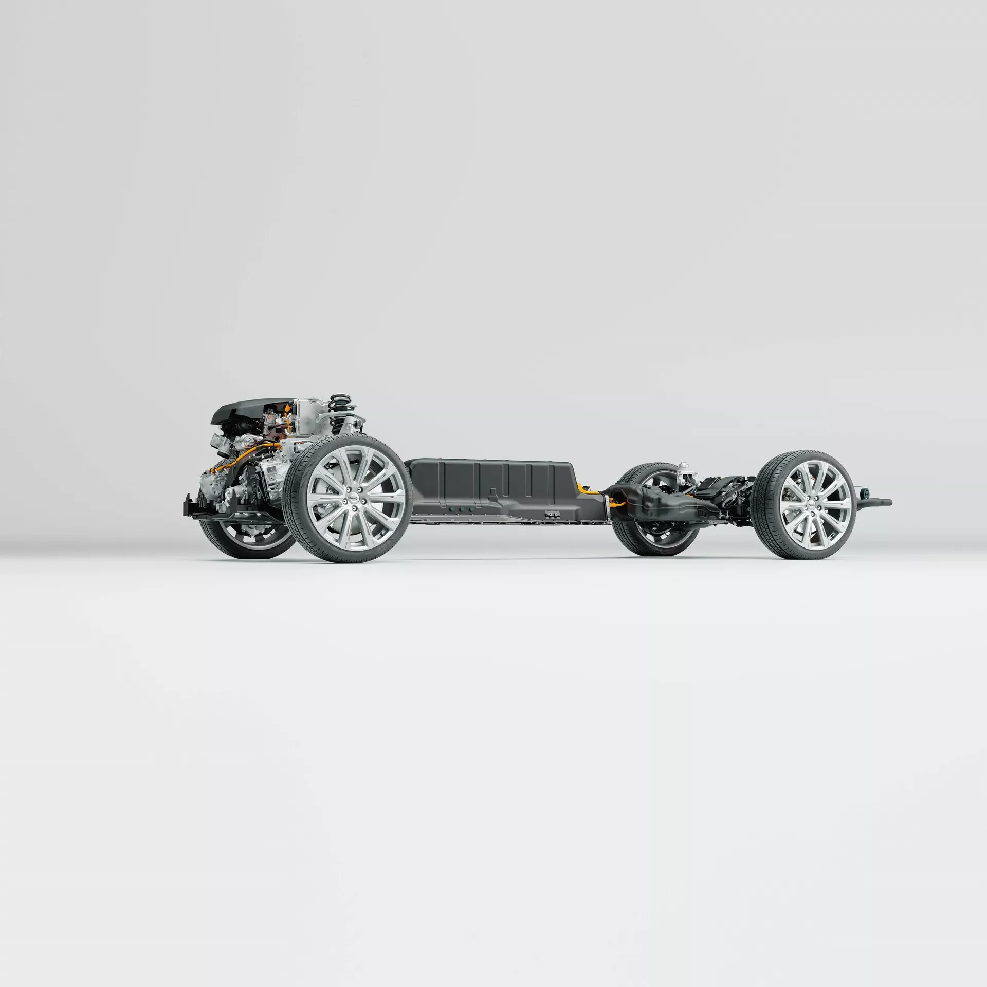 A 2021-es Volvo XC60 (2. generációs facelift) gördülő alvázának oldalsó profilja. A kép kiemeli a jármű vázát, modern ötvözet felnikkel felszerelt kerekeket, felfüggesztés alkatrészeit, elülső motorhajtóművet és központi akkumulátorcsomagot, mindez tiszta, semleges háttér előtt. A fotó bonyolult részleteket tár fel a fejlett mérnöki munkából, karosszéria vagy belső alkatrészek nélkül.