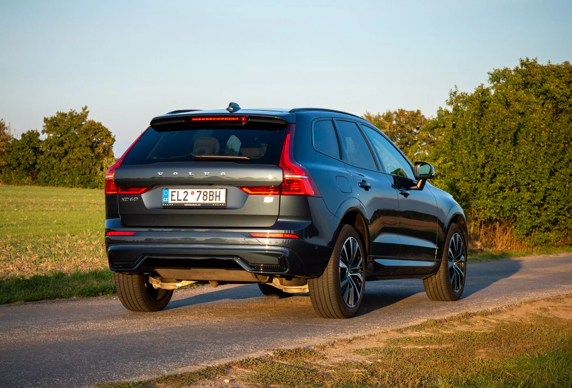 2021-es Volvo XC60 Recharge plug-in hibrid SUV háromnegyedes hátsó nézetben parkol egy országúton az aranyórában, látható a jármű hátsó része, az utasoldal, a csomagtartó részletei és a tervezési jellemzők