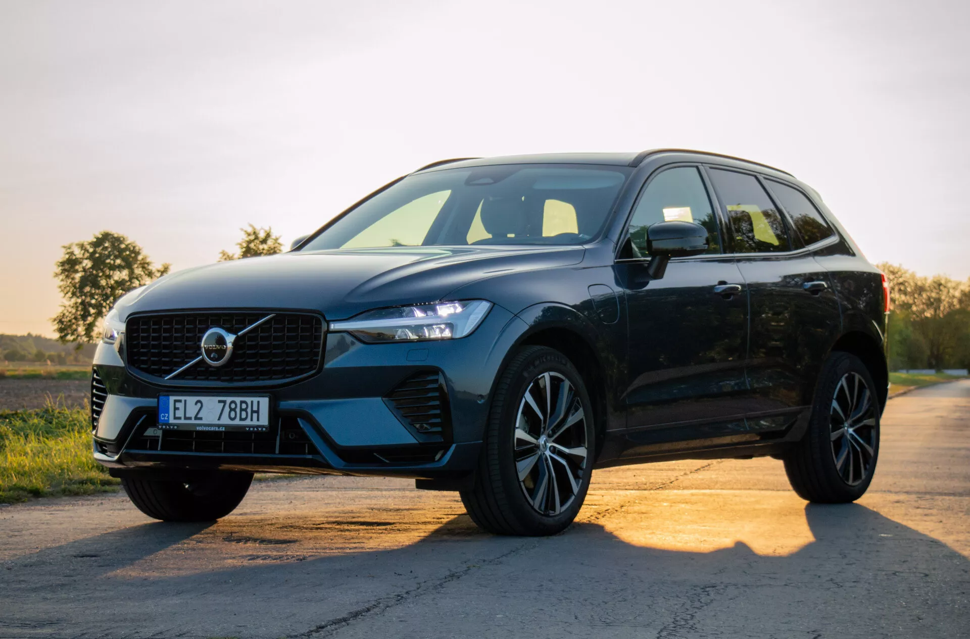 Fekete, modern SUV Volvo XC60 Recharge Plug-in Hybrid 2021, aszfaltúton parkolva napkelte vagy napnyugta idején, bemutatva a designját a rácsra, LED fényszórókra, ötvözött kerekekre és oldalnézetre koncentrálva egy gradiens ég háttérrel
