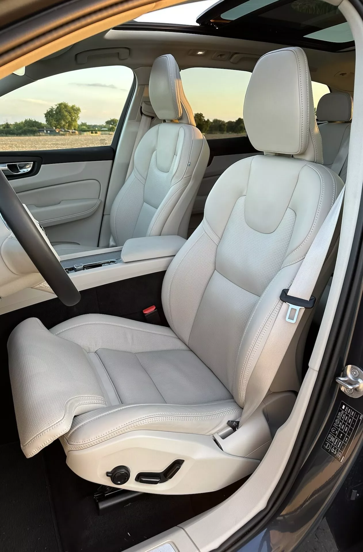 2021-es Volvo XC60 Recharge plug-in hibrid belső nézet: első és részleges hátsó ülések, luxus világosszínű bőrkárpit, modern design, elektromosan állítható ülések elegáns varrásvonalakkal, a jármű utasoldali ajtaján kívülről készült fénykép napfényben