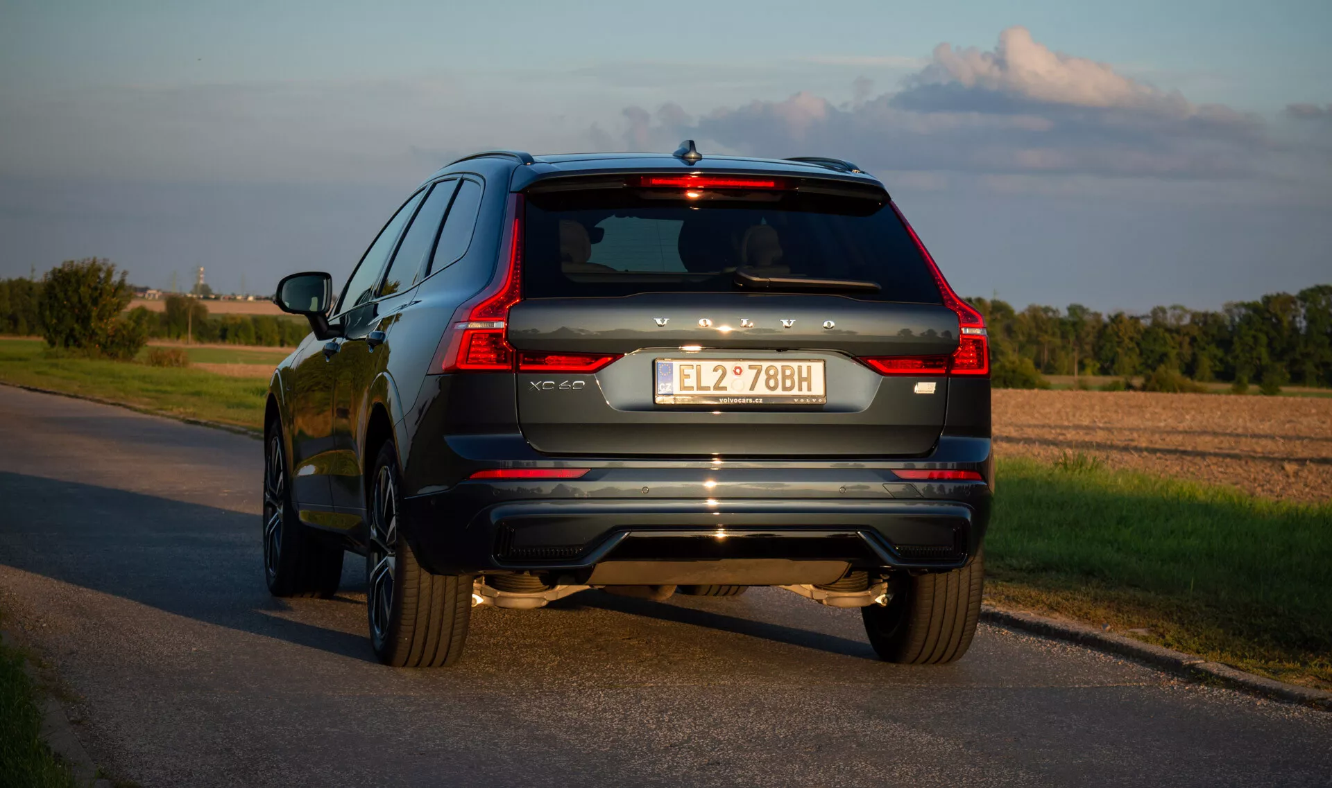 2021-es Volvo XC60 Recharge plug-in hibrid SUV aszfaltúton, hátulról háromnegyedes szögben készült felvétel, amely kiemeli a jármű LED hátsó lámpáit, kipufogó rendszerét és króm díszítéseit késő délután