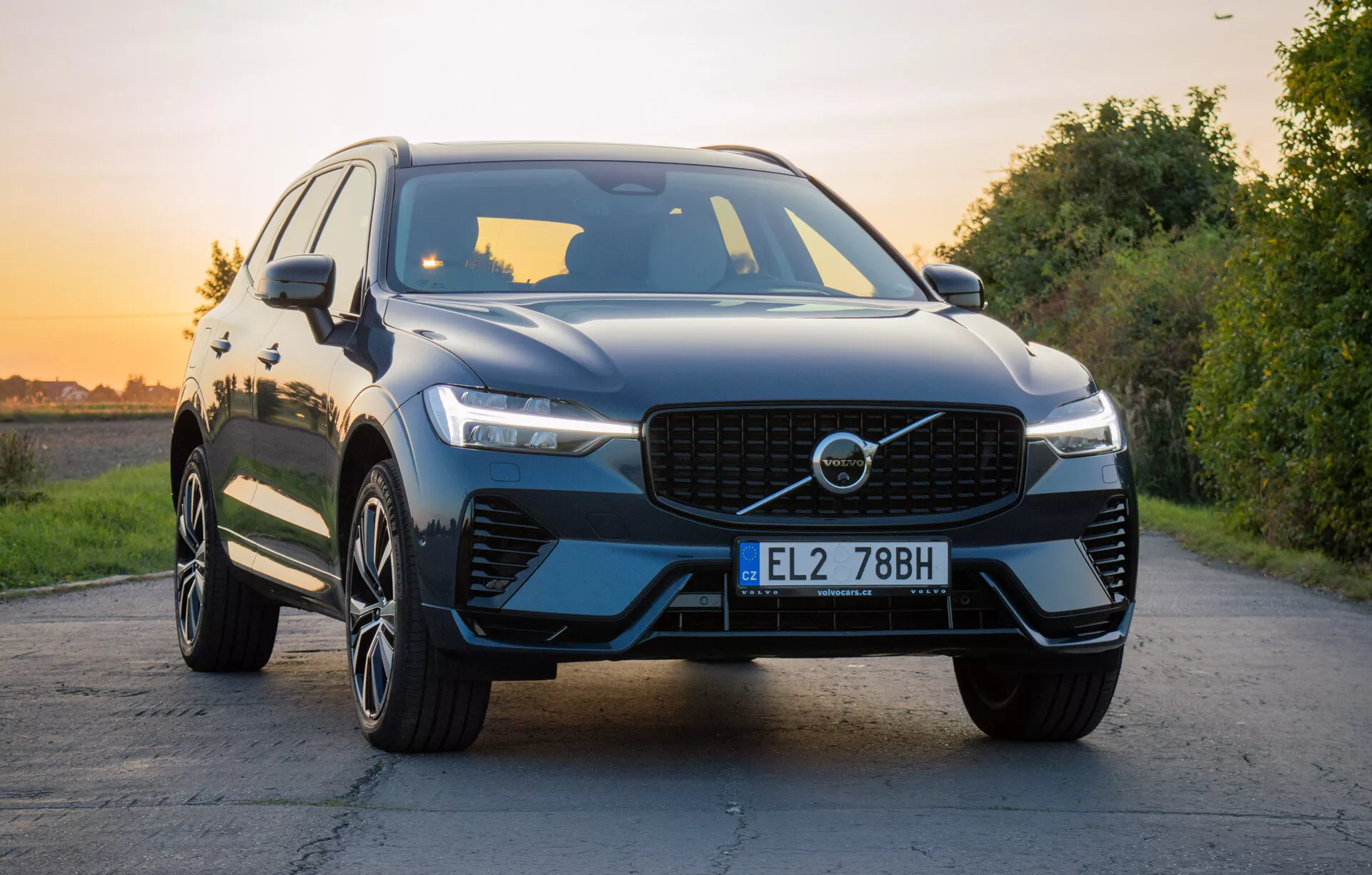 2021-es Volvo XC60 Recharge Plug-In Hybrid luxus SUV természetes tájjal a háttérben aranyóra alatt, bemutatva az első hűtőrácsot, LED fényszórókat, faragott motorháztetőt, többsugaras ötvözött kerekeket és fényes bevonatot