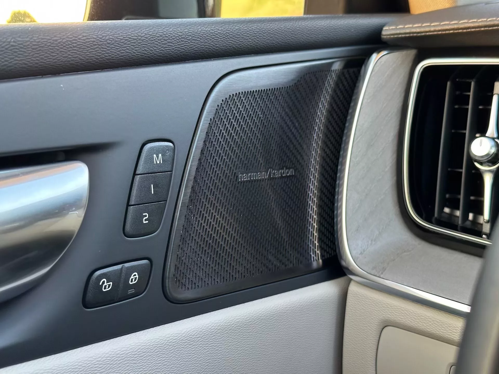 A 2021-es Volvo XC60 Recharge Plug-In Hybrid belső nézete a vezető oldali ajtópanelre összpontosítva, amely a memóriaülés-beállításokat, az elektronikus ajtózár-vezérlőket, egy harman/kardon hangszórórácsot és a műszerfal szellőzőrácsának egy részét mutatja