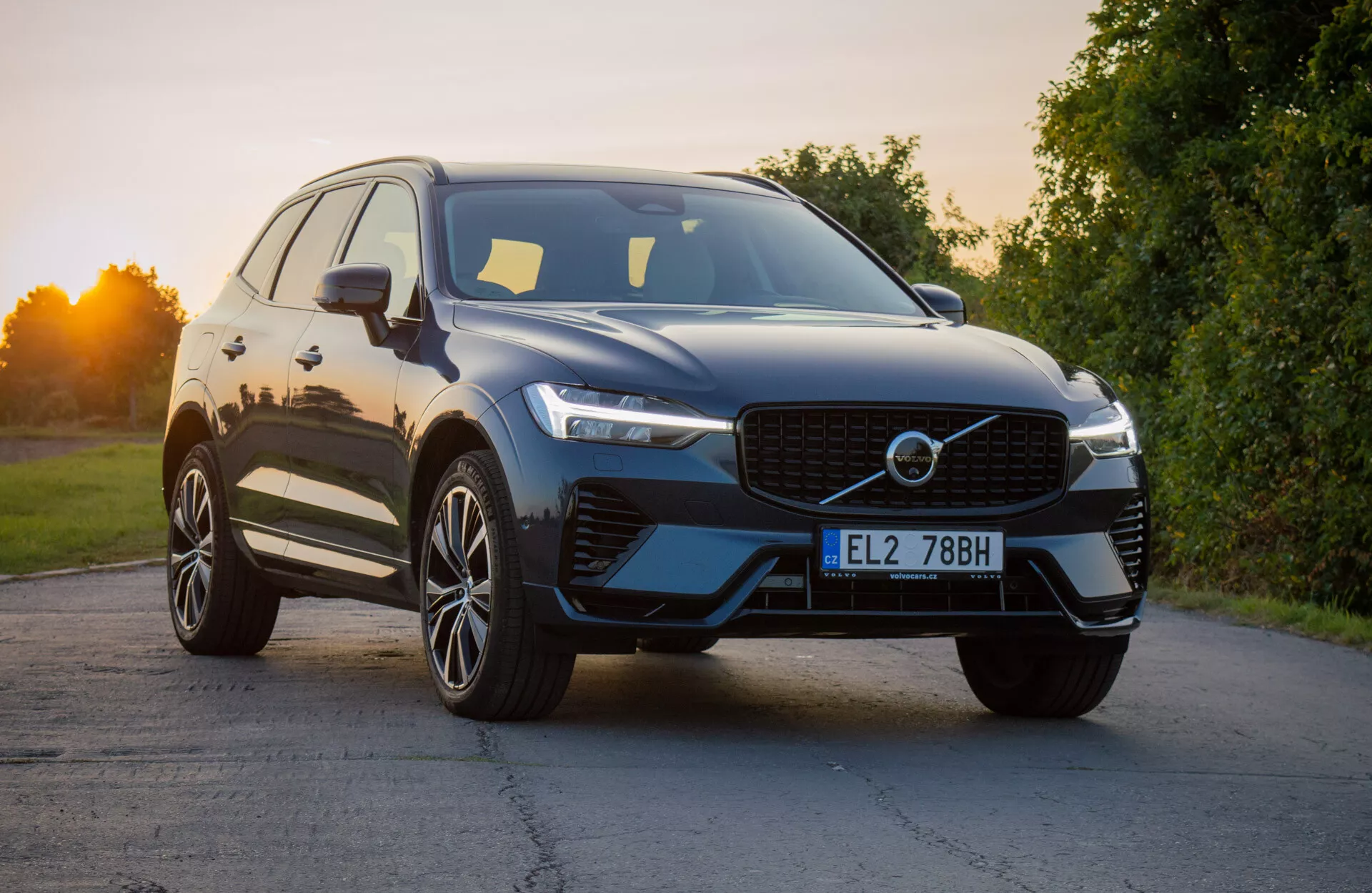 2021-es Volvo XC60 Recharge Plug-In Hybrid modern SUV kialakításban, enyhén szögben pozicionálva a jármű első negyedének kiemelésére, bemutatva a jellegzetes hűtőrácsot, a karcsú LED fényszórókat és az aerodinamikus első lökhárítót integrált légbeömlőkkel, kiegészítve fényes külső felülettel és prémium többsugaras ötvözött kerekekkel természetes nappali fényben.