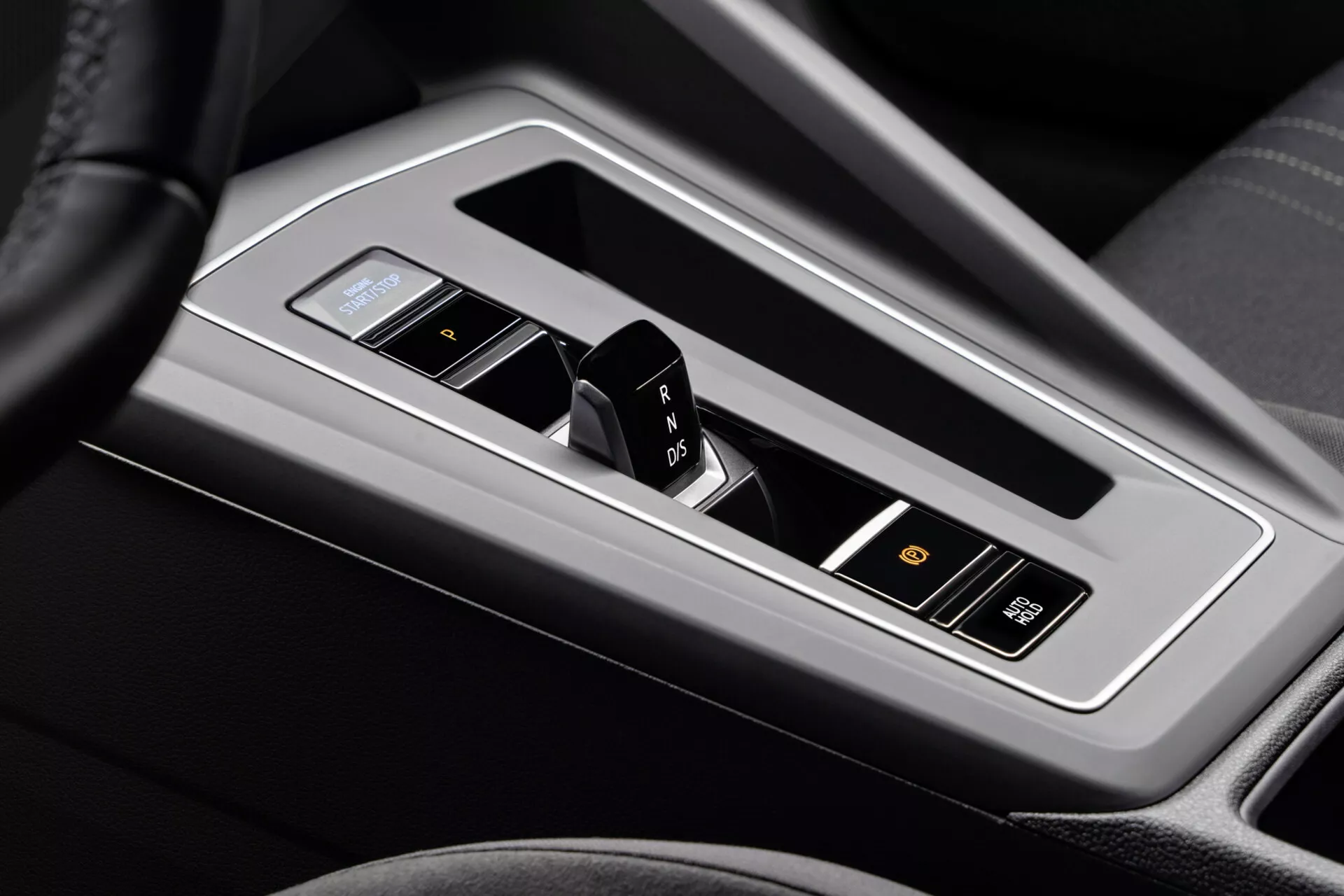 A 2017-es VW Golf Alltrack középkonzoljának közelképe, amely kiemeli az automatikus sebességváltó karját fényes fémborítással és elektronikus kijelzővel, fekete bőr vagy műbőr környezetében, felszerelve sebességjelzőkkel, sport móddal és haladó vezetői segédrendszerek gombokkal.