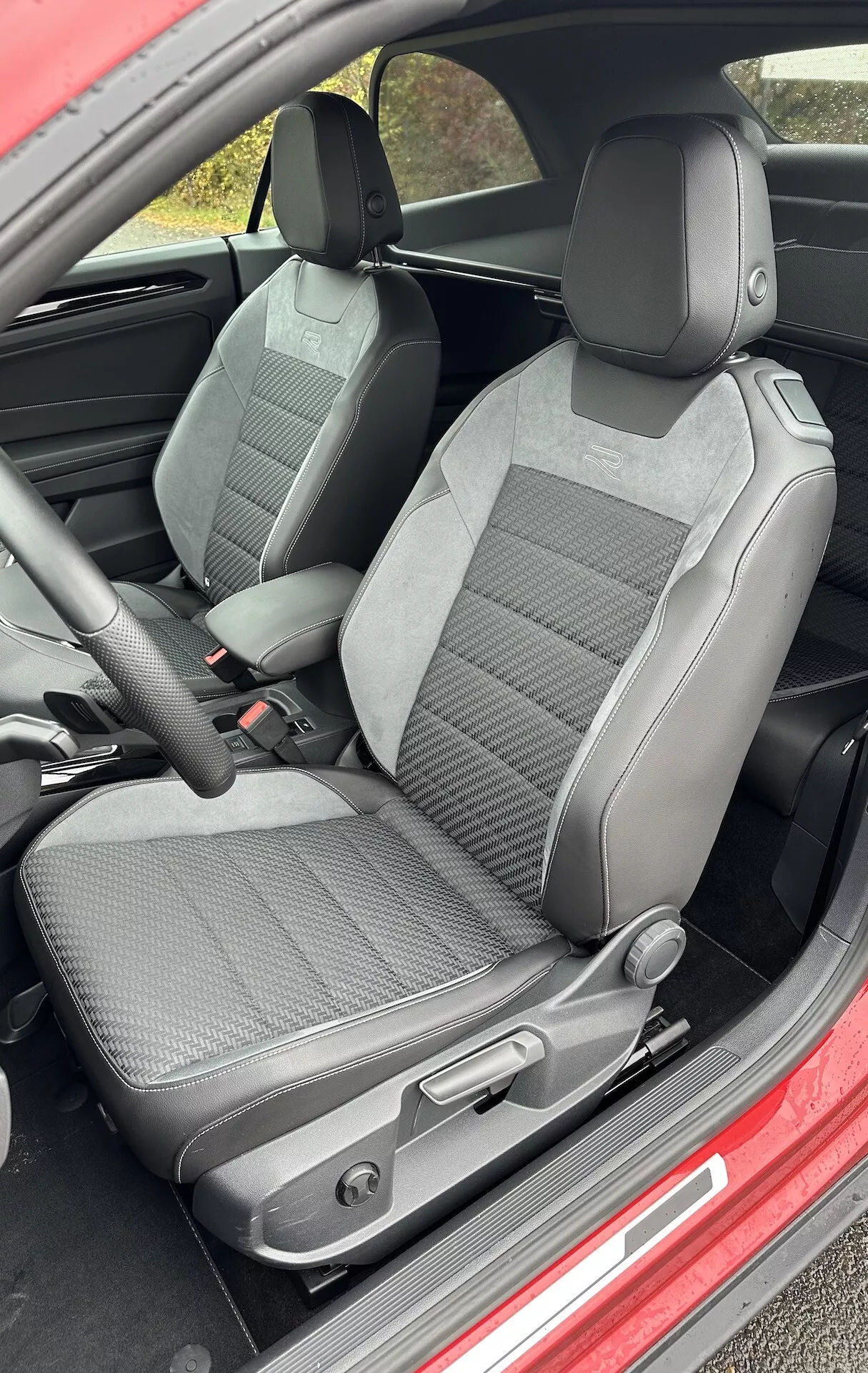 A 2022-es VW T-Roc Cabriolet belső nézete, amely a vezető és az utas első üléseire összpontosít, két árnyalatú szövet kárpittal, állítható fejtámlákkal, kézi ülésállító szabályzókkal és kiemelkedő oldalsó támaszokkal az erősített támogatás érdekében.