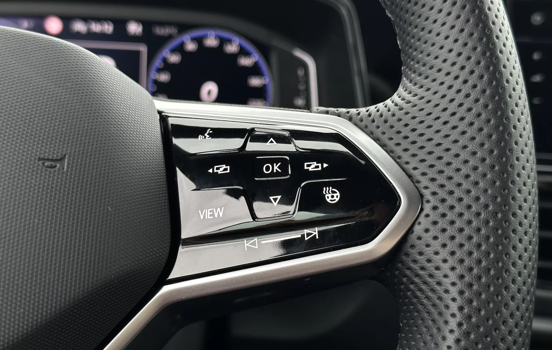 Közeli kép a 2022-es VW T-Roc Cabriolet multifunkciós kormánykerék vezérlőiről, ergonomikus kialakítást és az infotainment rendszer valamint a jármű beállításaihoz tartozó interaktív gombokat bemutatva