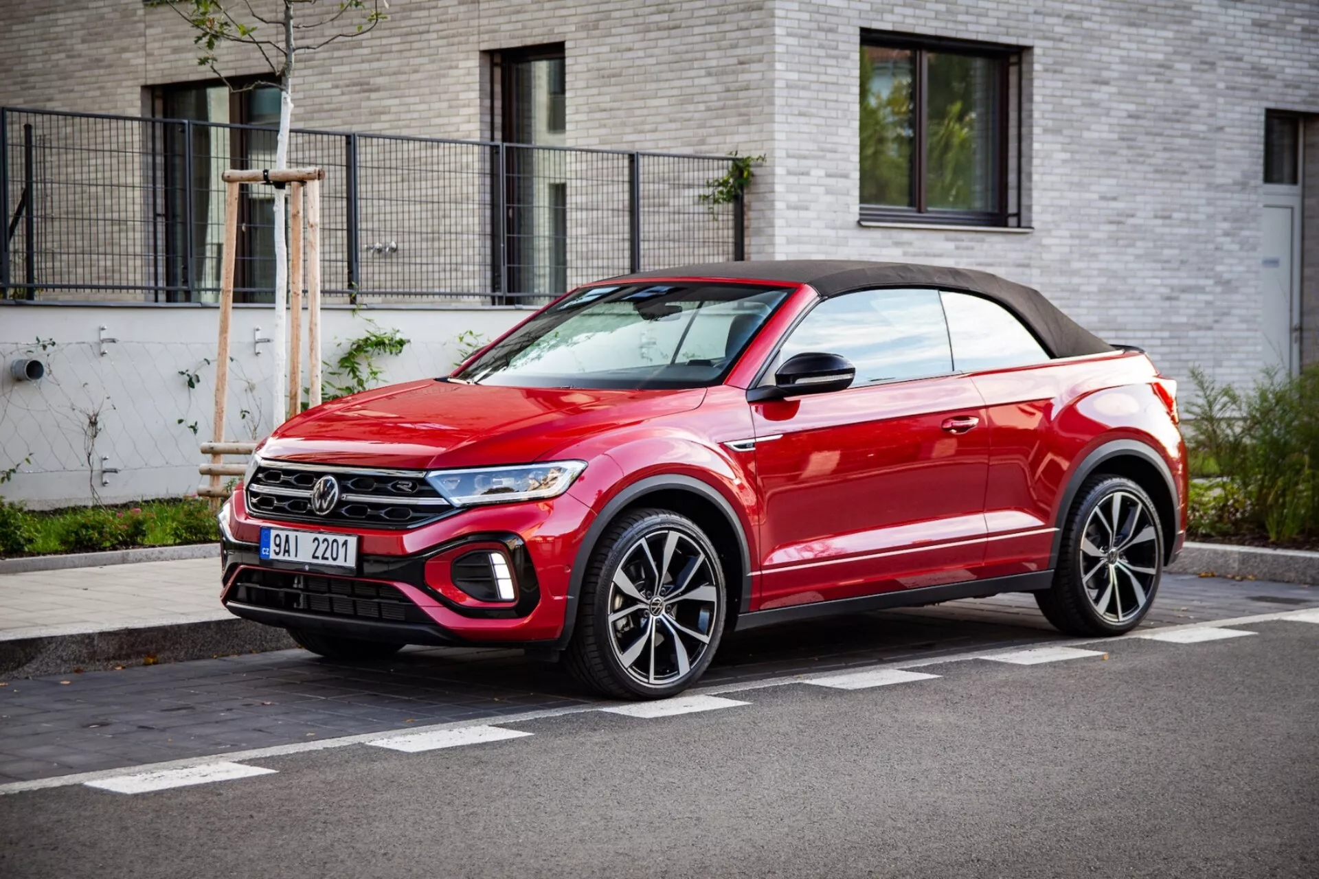 Világos piros VW T-Roc Cabriolet crossover kabrió SUV parkol az út szélén, bemutatva az első hűtőrács, LED fényszórók, ötvözetkerékek, és puha tetejét, tiszta időben háromnegyedes első nézetben