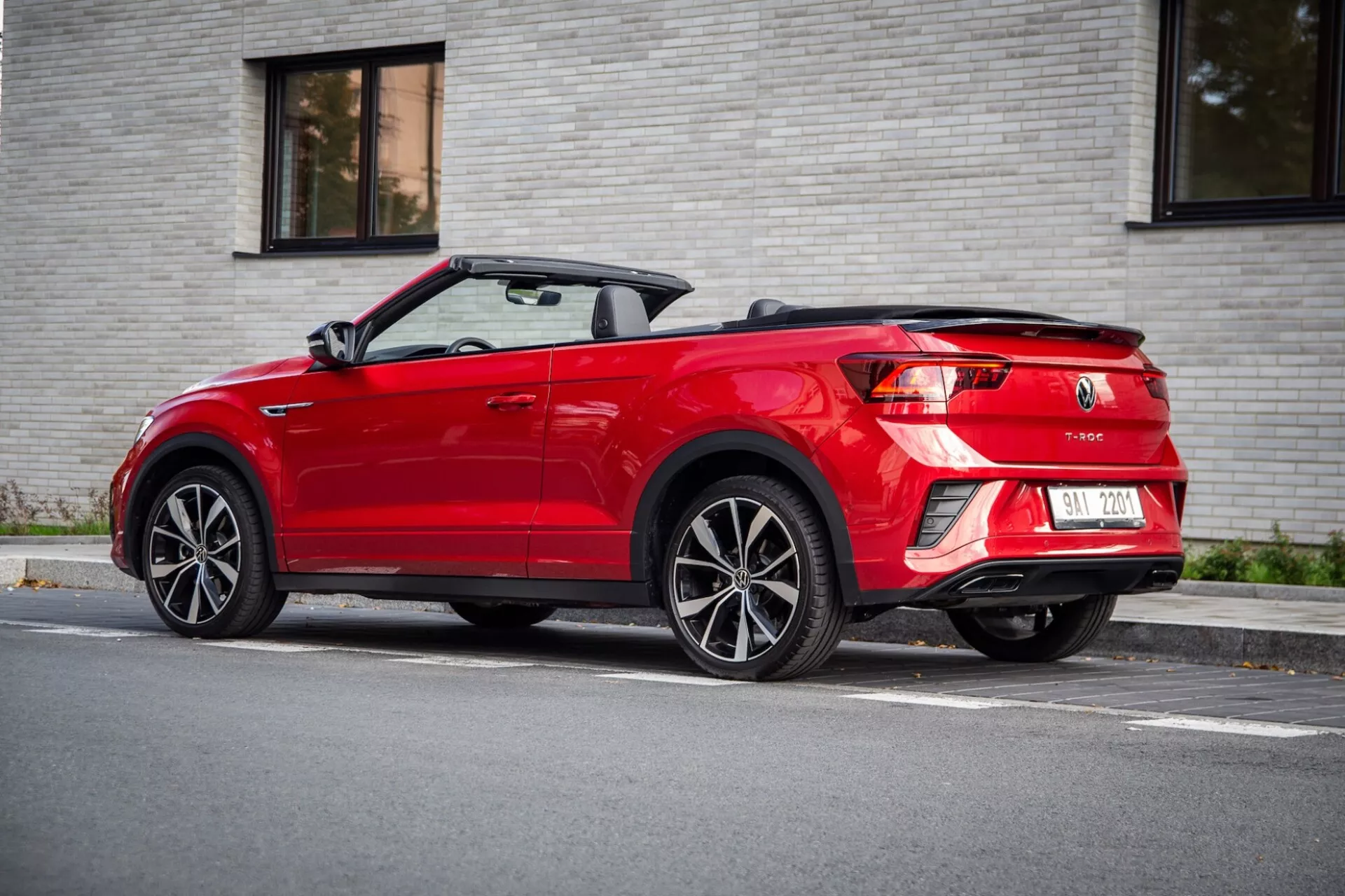 Háromnegyedes hátsó nézet egy 2022-es piros VW T-Roc Cabriolet-ről, visszahúzott puha tetővel, LED hátsó lámpákkal, kettős kipufogóval és több küllős könnyűfém kerekekkel, napfényes utcán parkolva